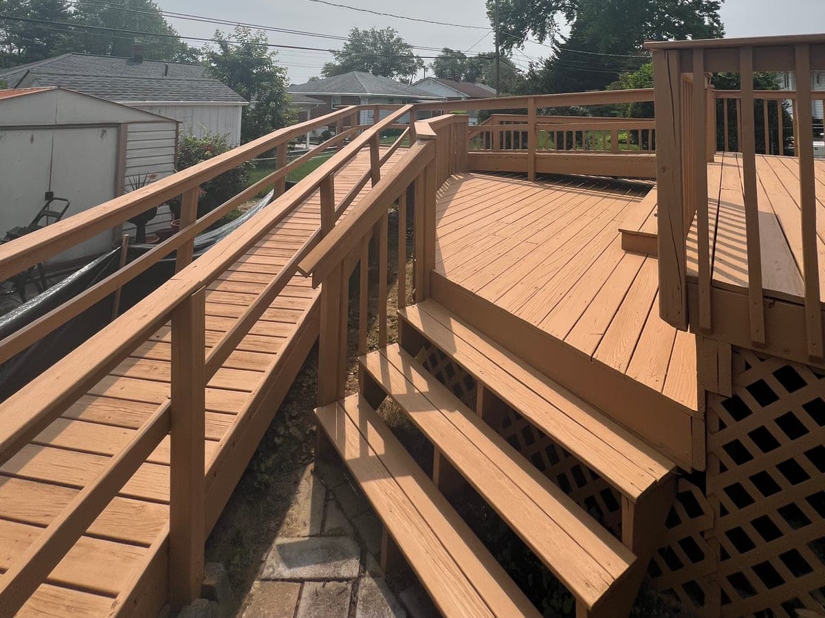 Freshly stained deck in a cedar tone: boards, steps, ramp and rail