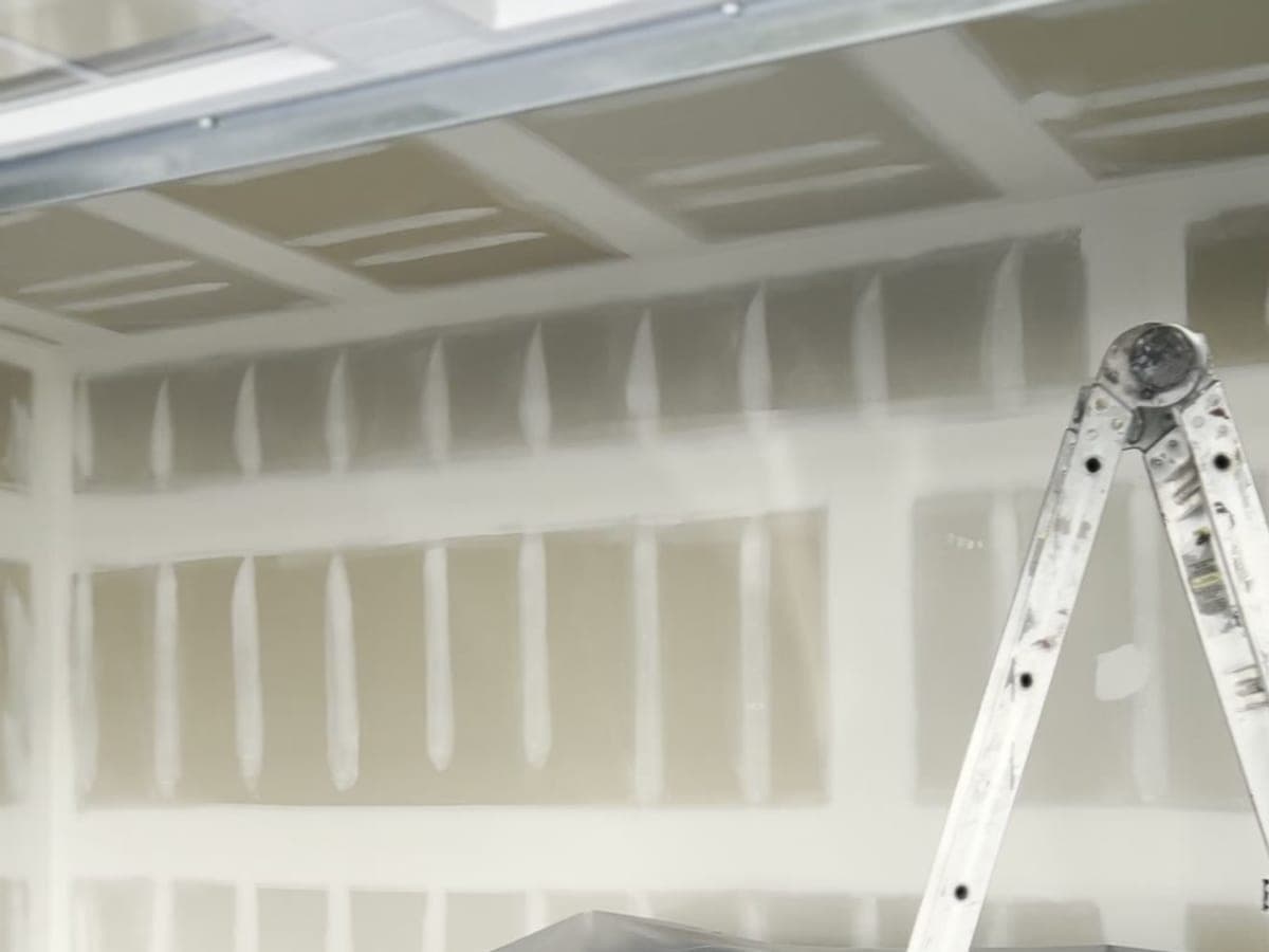 New-construction garage with every drywall joint taped and mudded, ladder at the wall