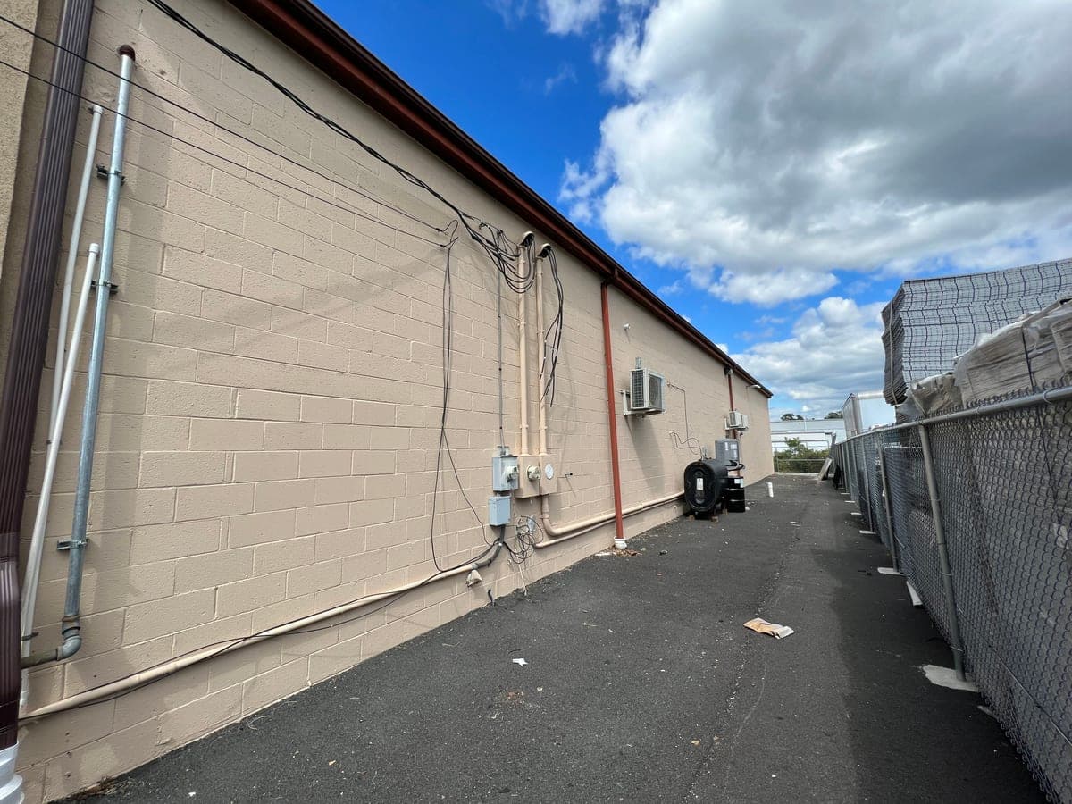 Long tan block commercial wall along an asphalt drive, conduit and meters, finished