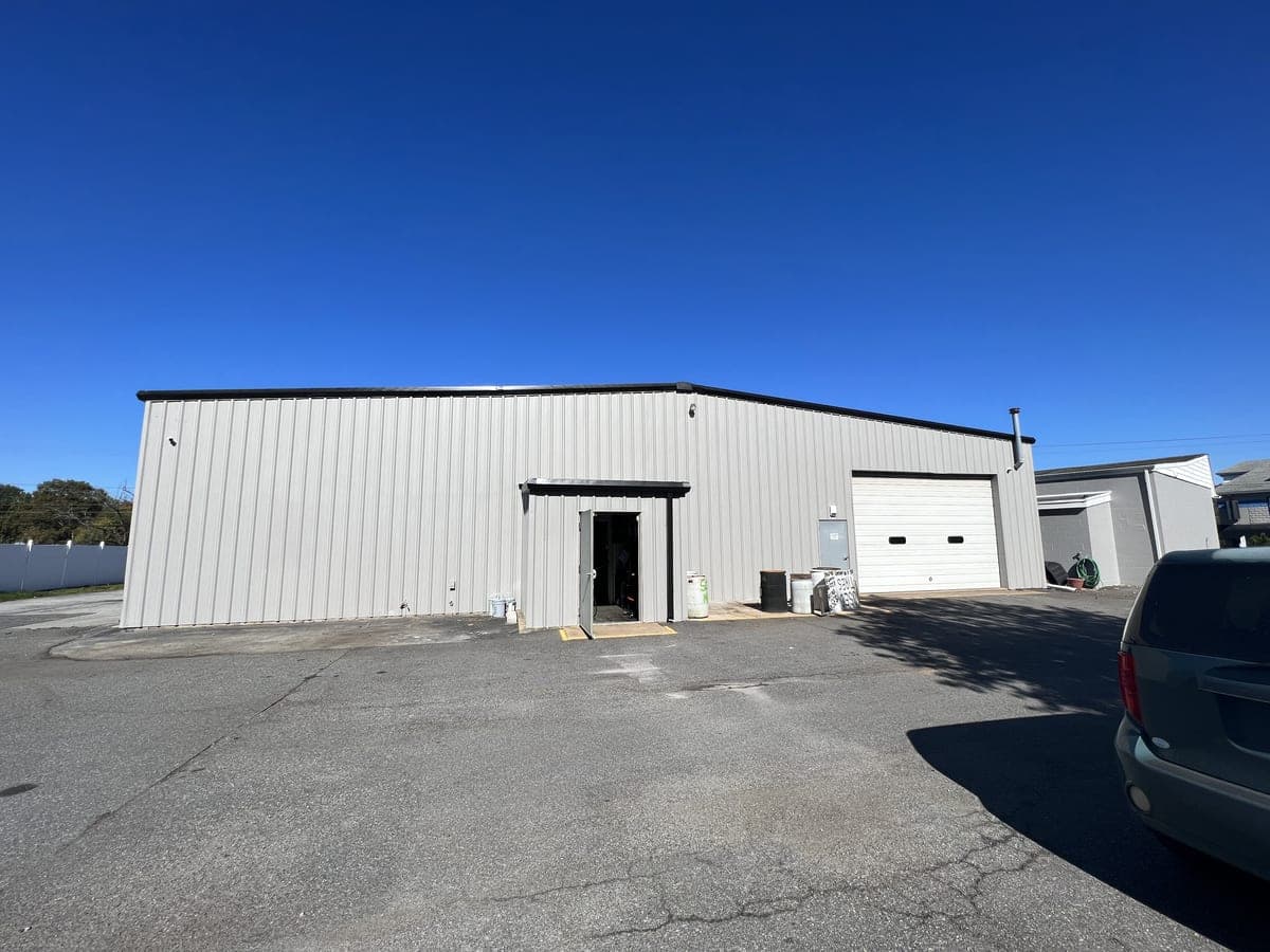 Long white metal building elevation with black trim, entry door and overhead door