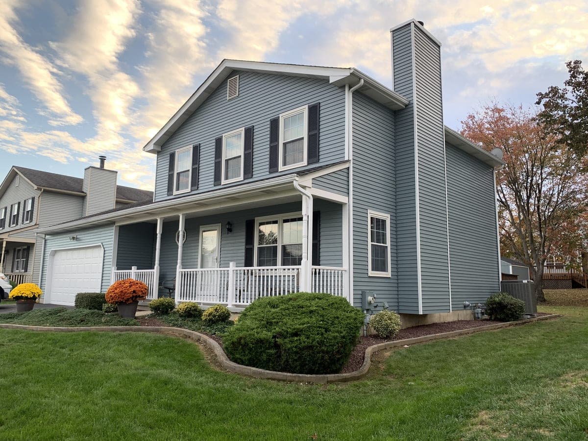 Blue-gray two-story with white porch rail and black shutters at golden hour