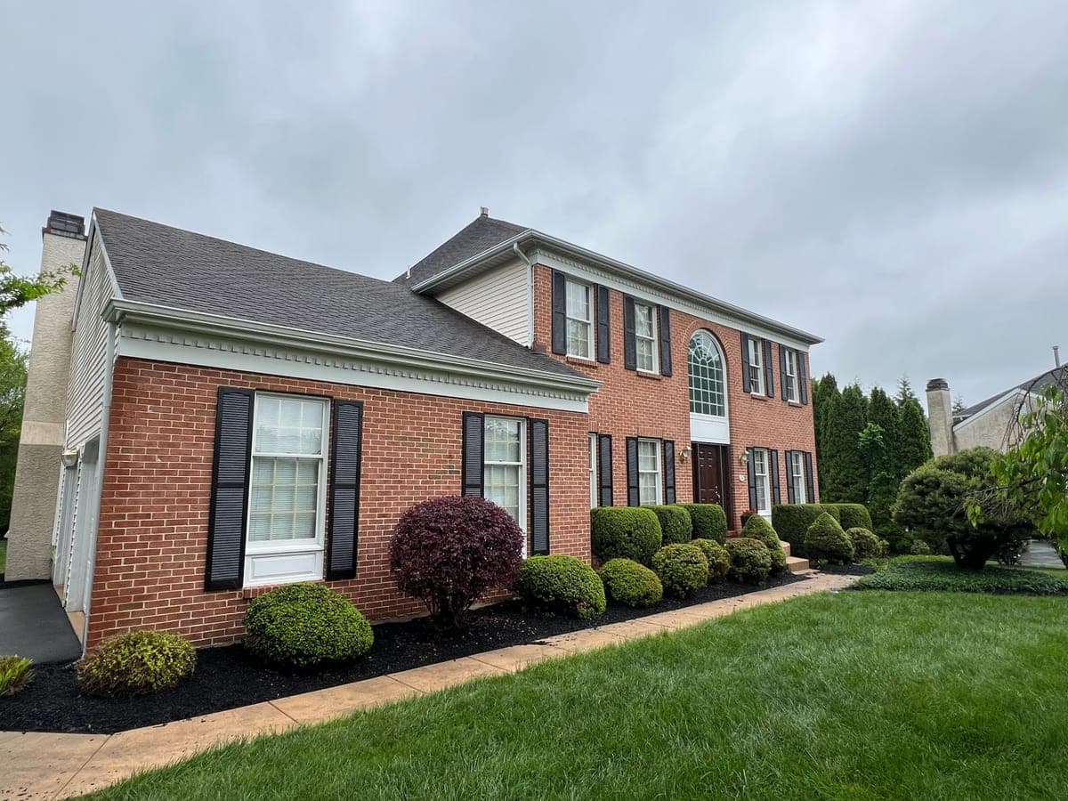 Red brick colonial front elevation with black shutters, cream trim and clipped shrubs