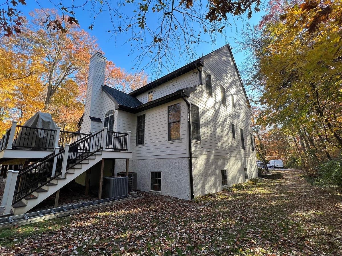 Rear of the same cream colonial: walkout basement, dark stained deck and stair, leaf-covered yard