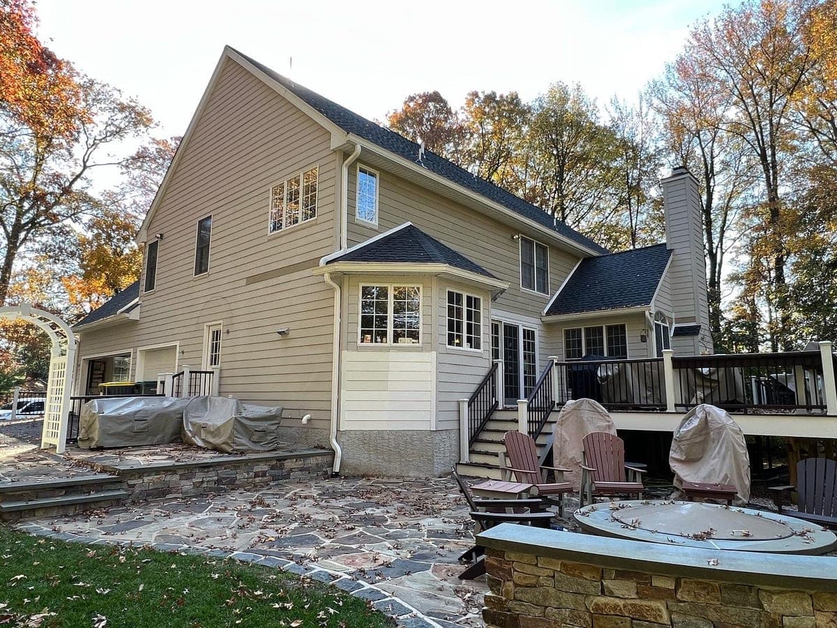 Side and rear of a cream house with stone fire pit patio, deck and sunroom, leaves down