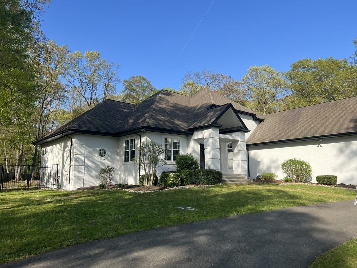 Full front of the cream stucco home with turret and long driveway