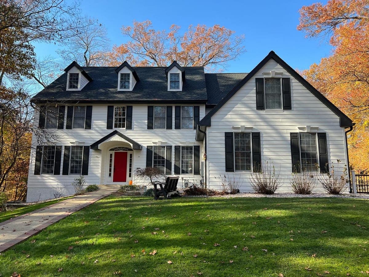 Front elevation of a white colonial with black shutters, red front door and dormers