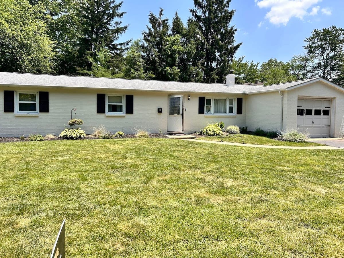 White painted brick ranch with black shutters and attached garage, large lawn