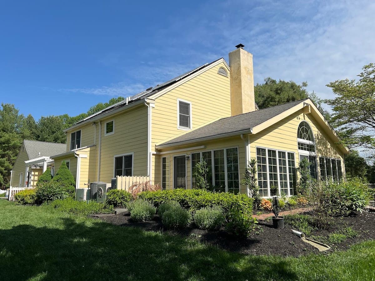 Yellow two-story home with white trim, sunroom addition and landscaped beds, exterior repaint