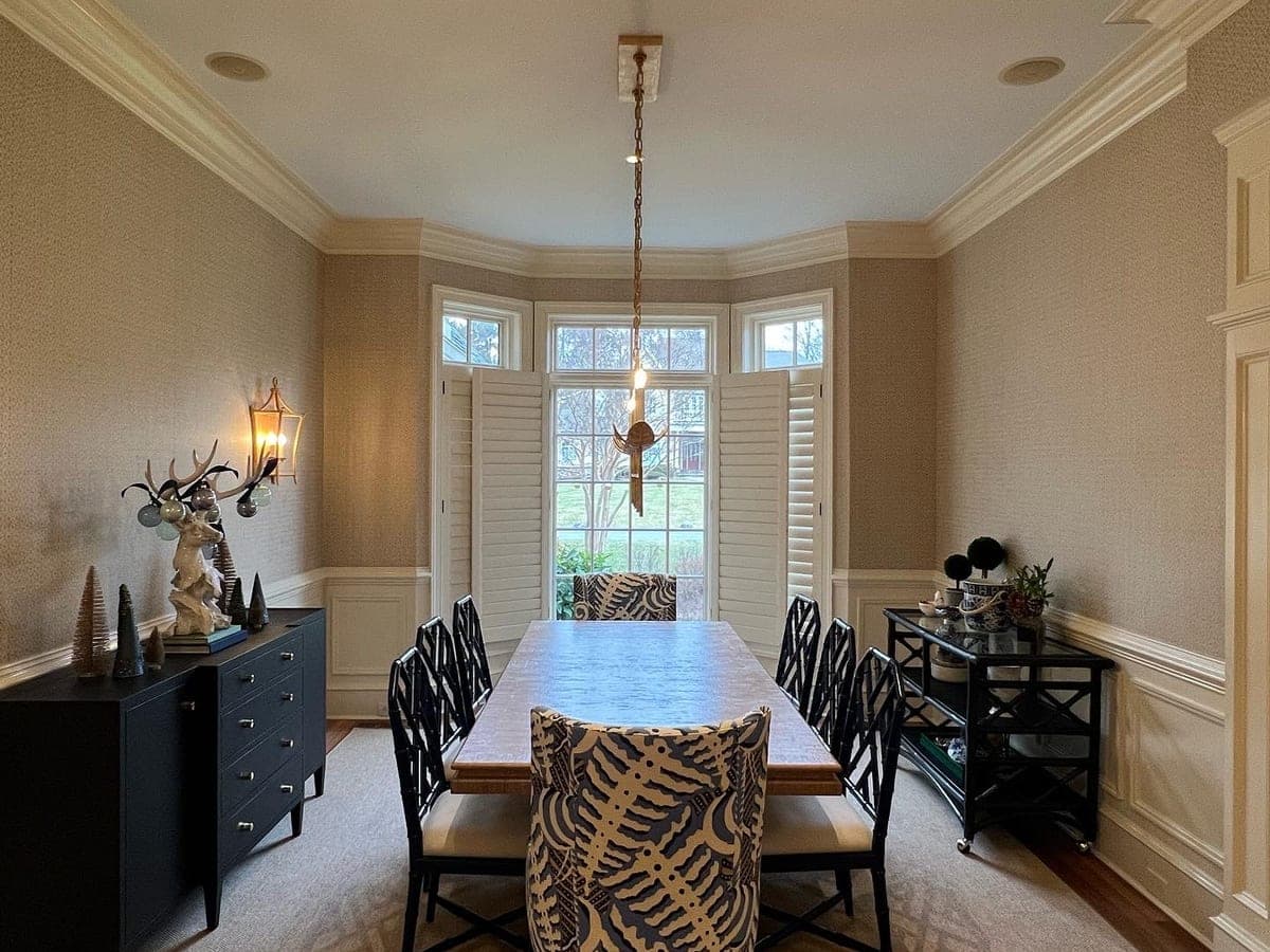 Formal dining room with grasscloth walls, cream trim and wainscot, bay window with shutters