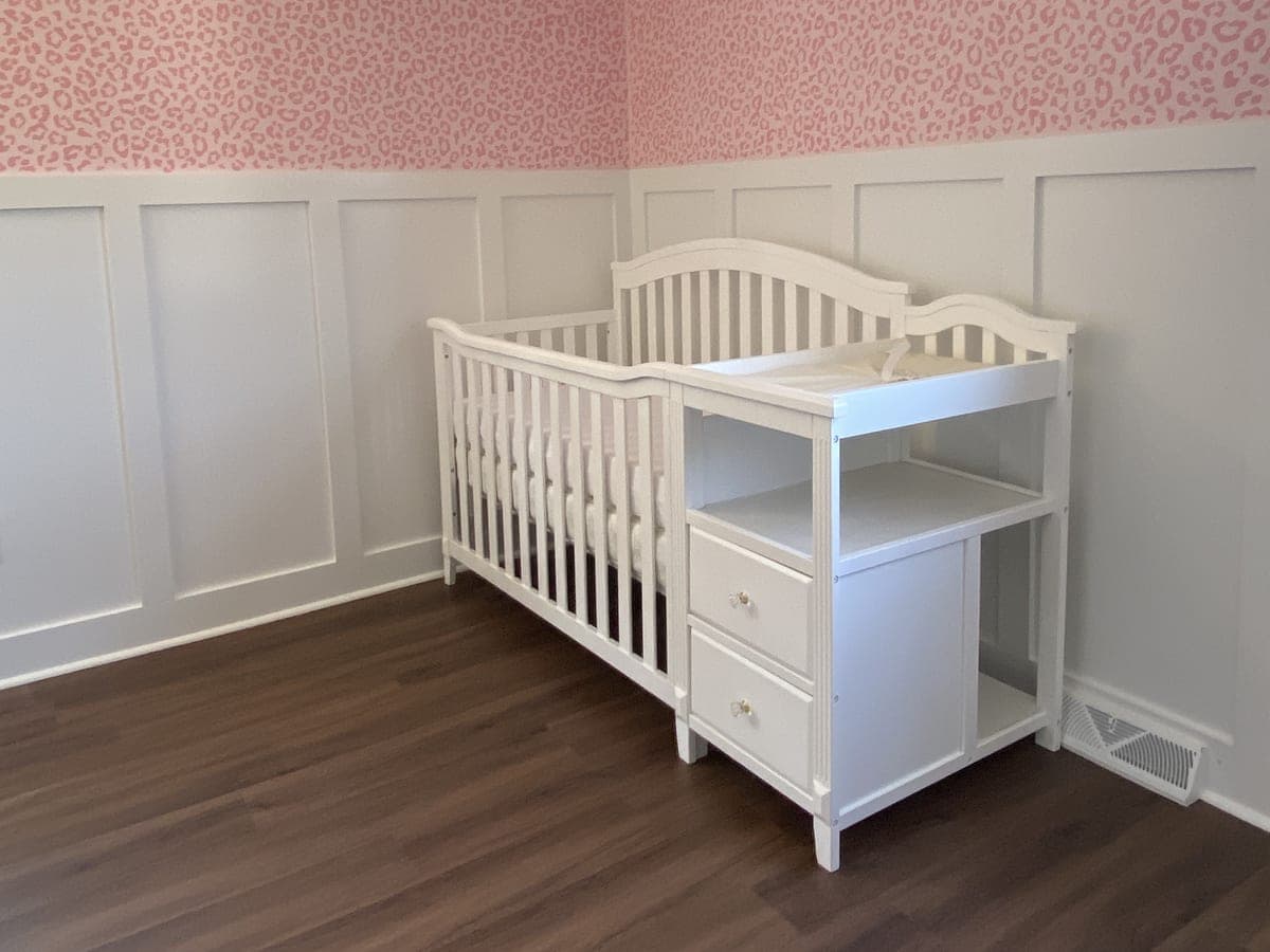 Finished nursery: pink leopard upper wall, white board-and-batten wainscot, crib and changing table