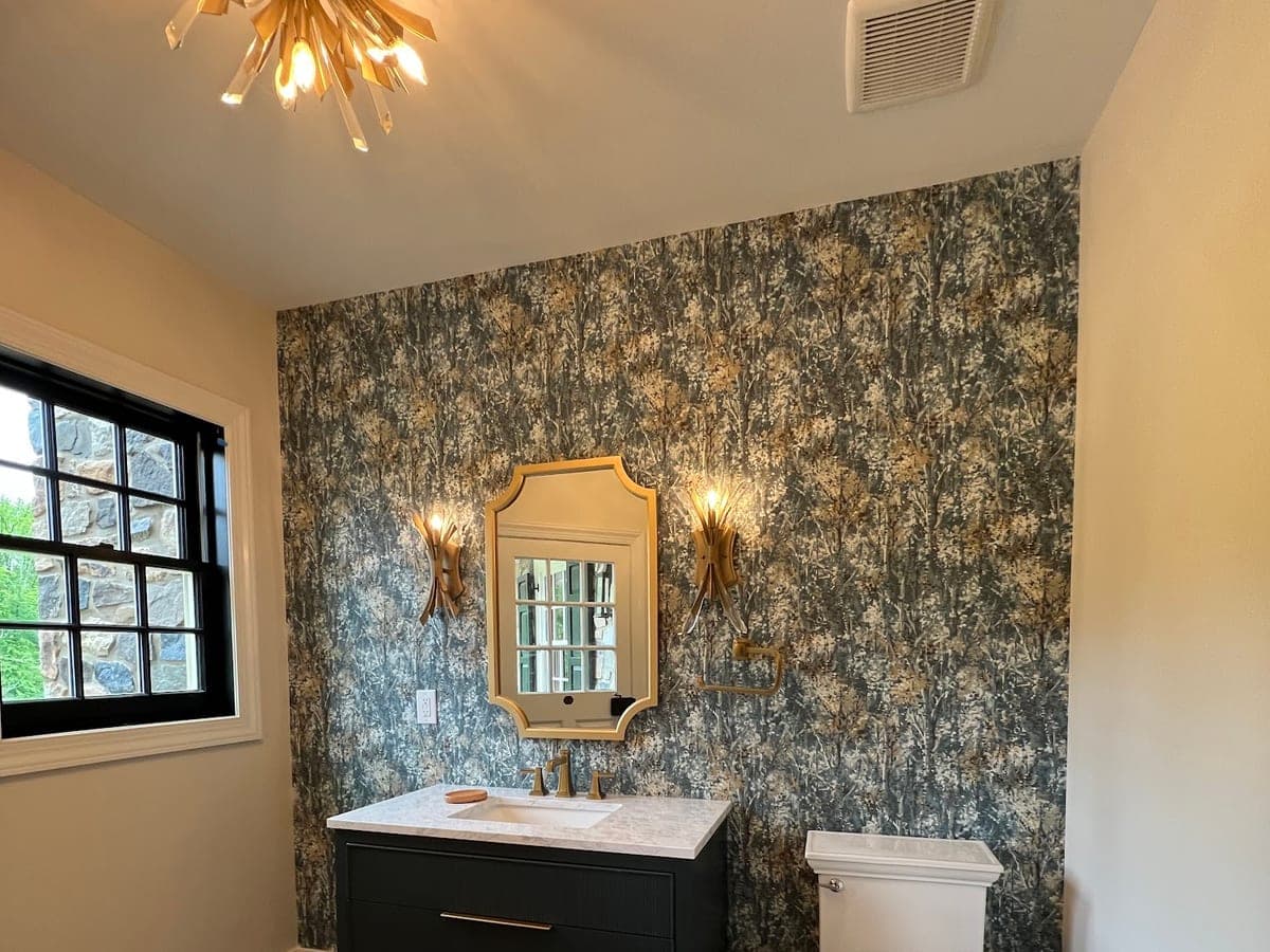 Powder room with botanical wallpaper feature wall, black vanity, brass sconces and mirror