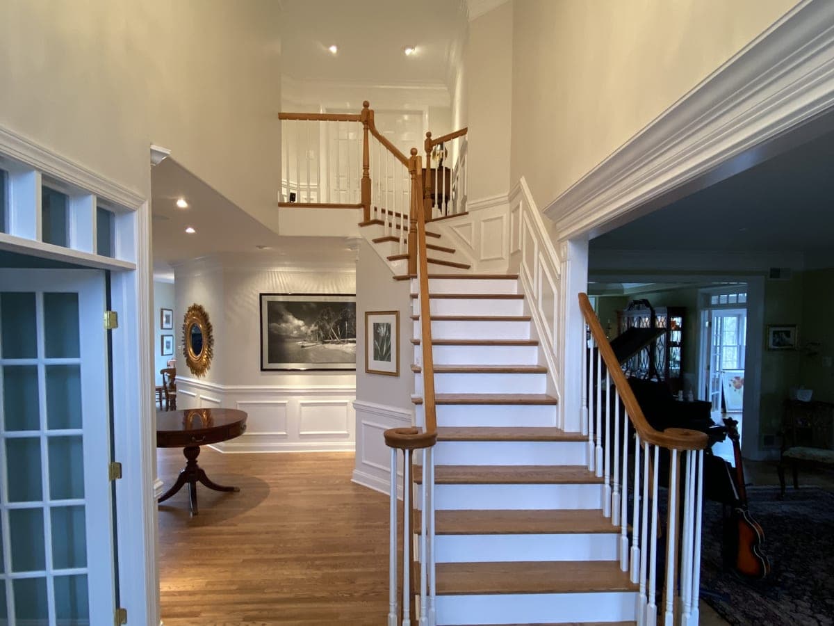 Two-story foyer with white staircase, oak rail and treads, white wainscot, brass chandelier