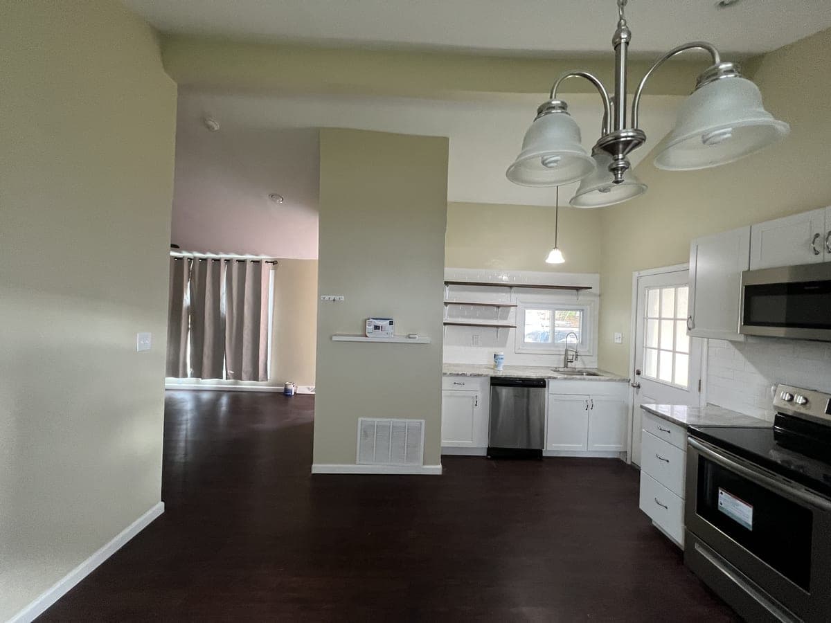 Open sage kitchen and living area in a new build with white cabinets and dark floor
