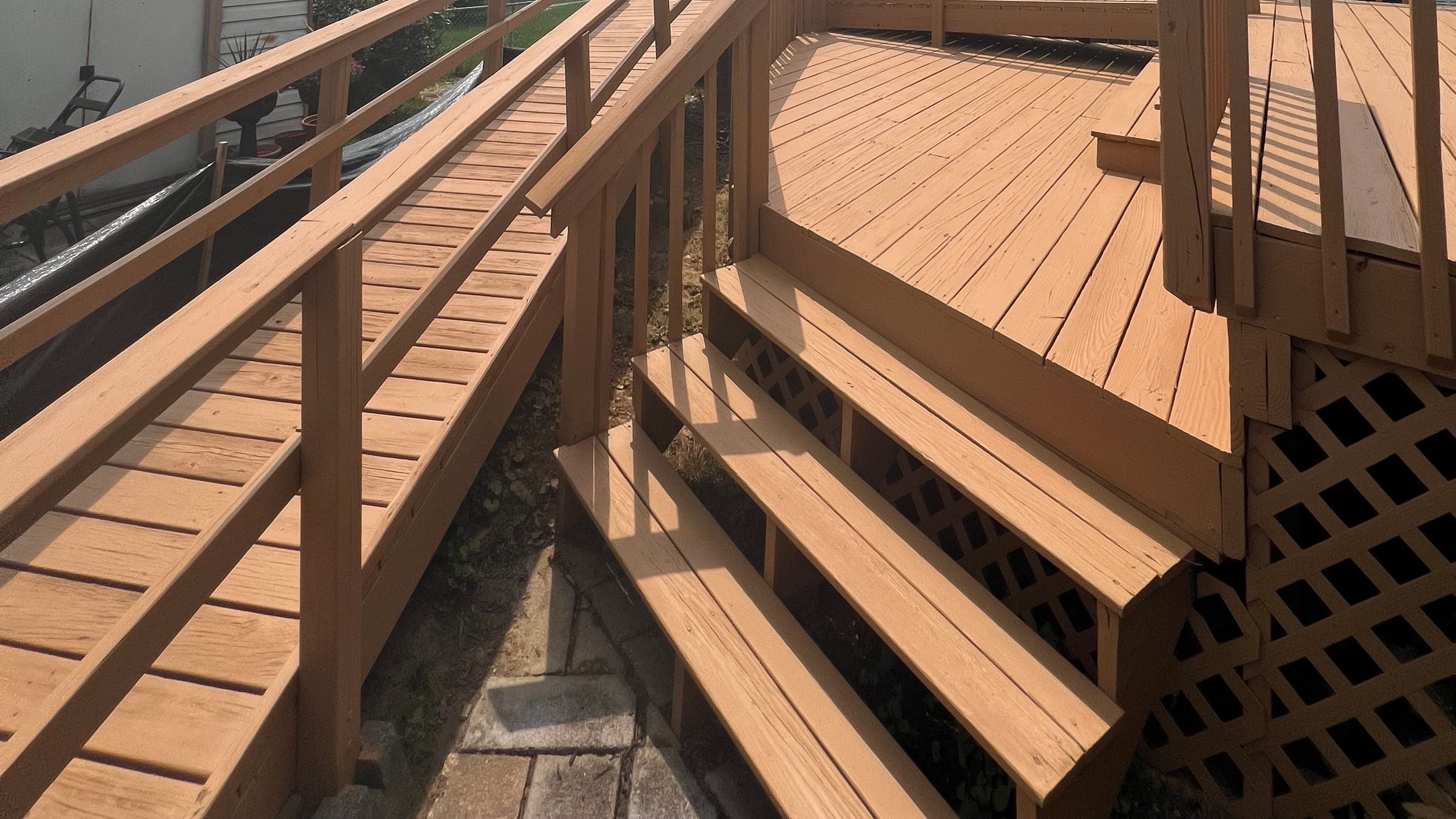 Freshly stained deck in a cedar tone: boards, steps, ramp and rail