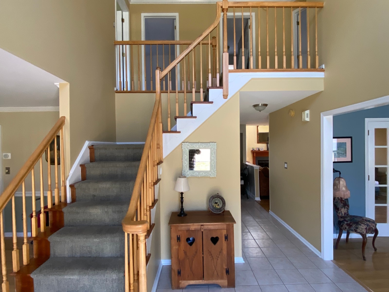 The same foyer finished: walls in warm beige with white trim, staircase uncovered, furniture back in place