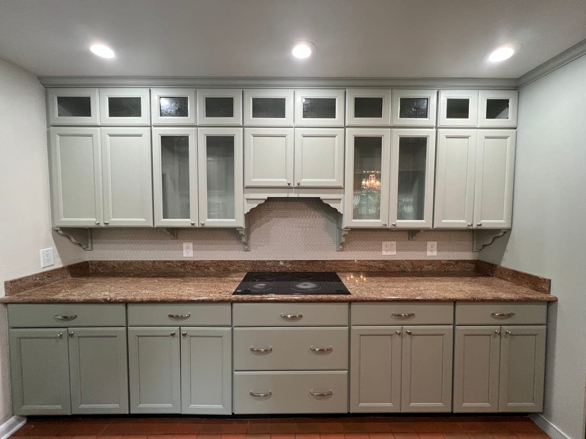 Kitchen cabinets painted sage green, with glass-front uppers and a granite counter