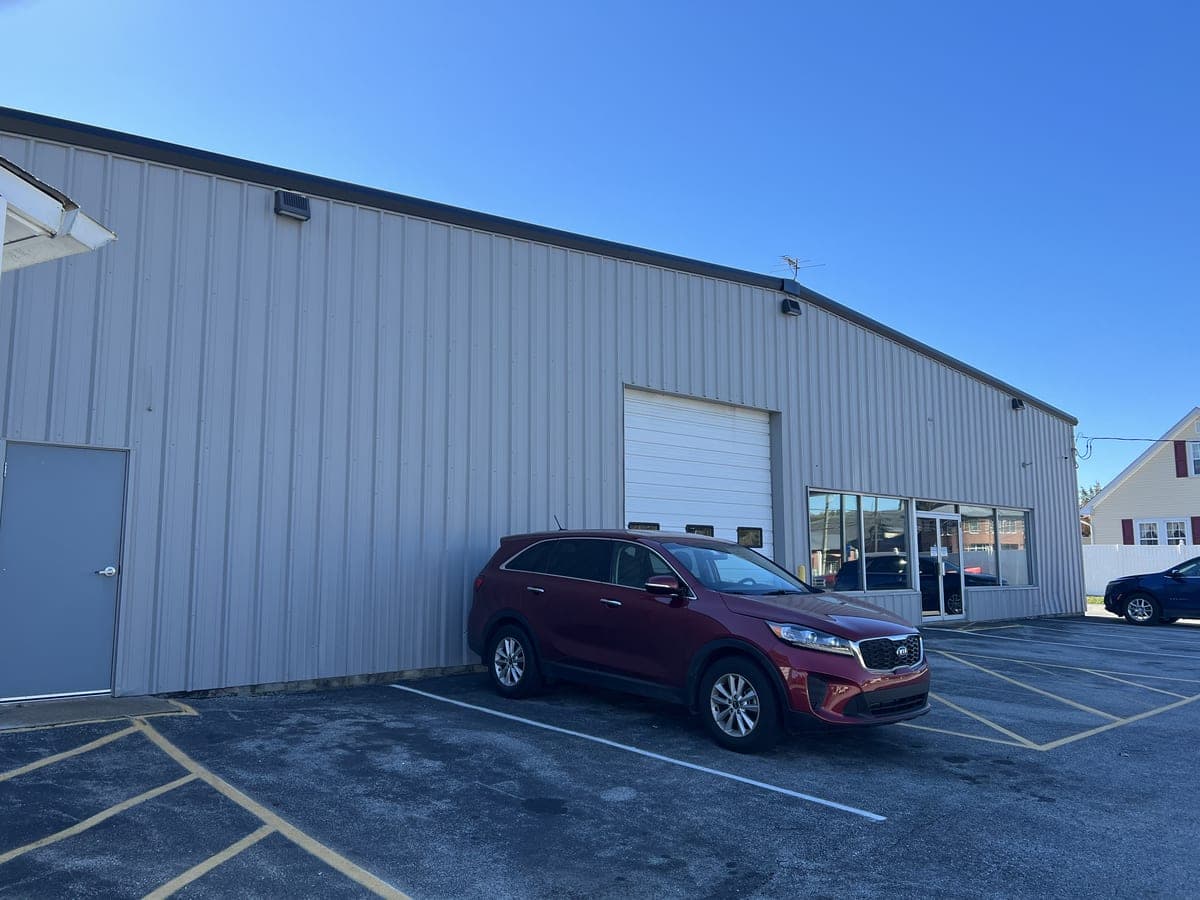 Finished white metal commercial building with overhead door, storefront windows and parked car
