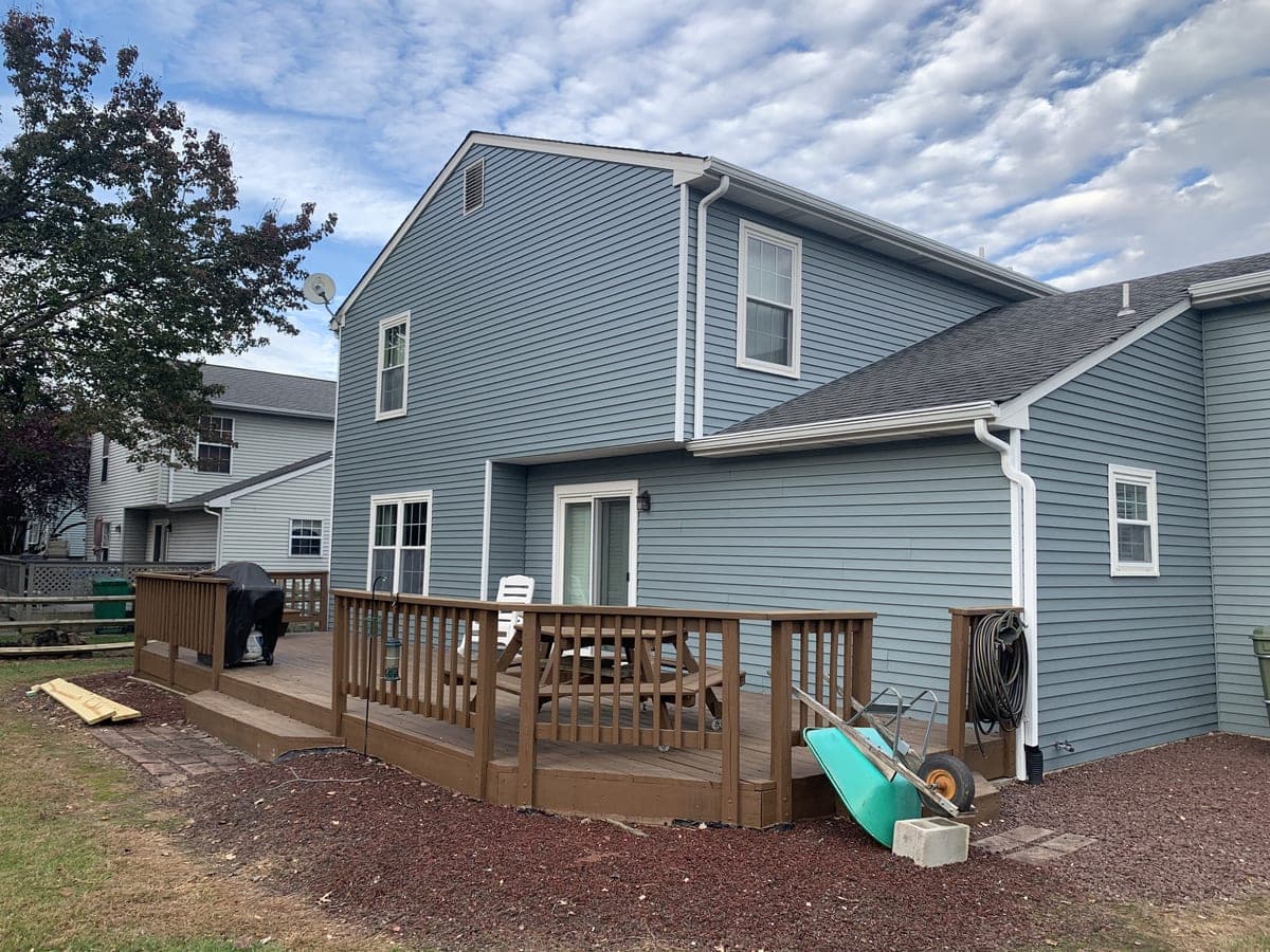 Blue-gray rear elevation with white trim, wood deck and open lawn