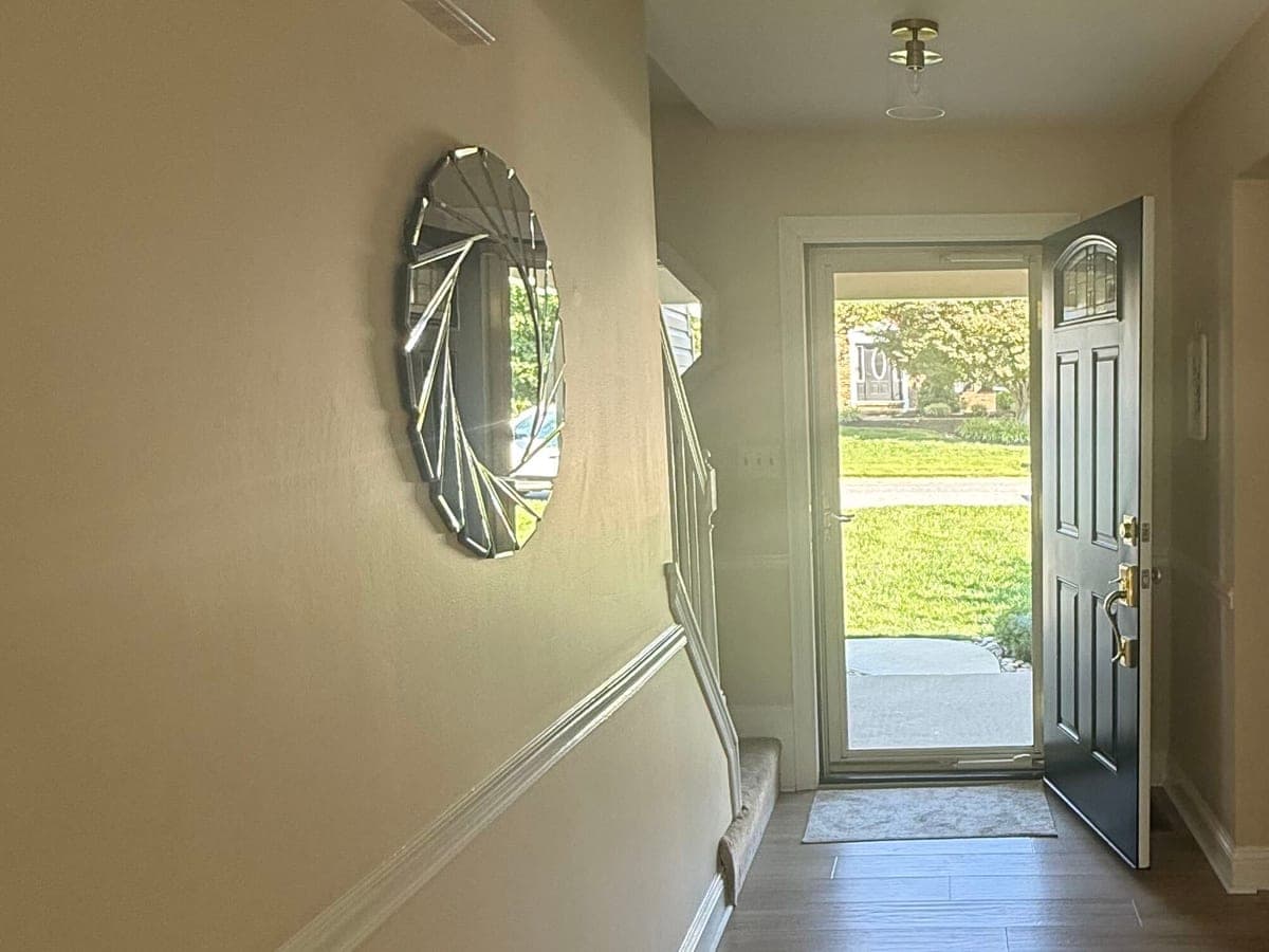 Front hall painted warm greige with white chair rail and trim, wood floor and the front door open to daylight