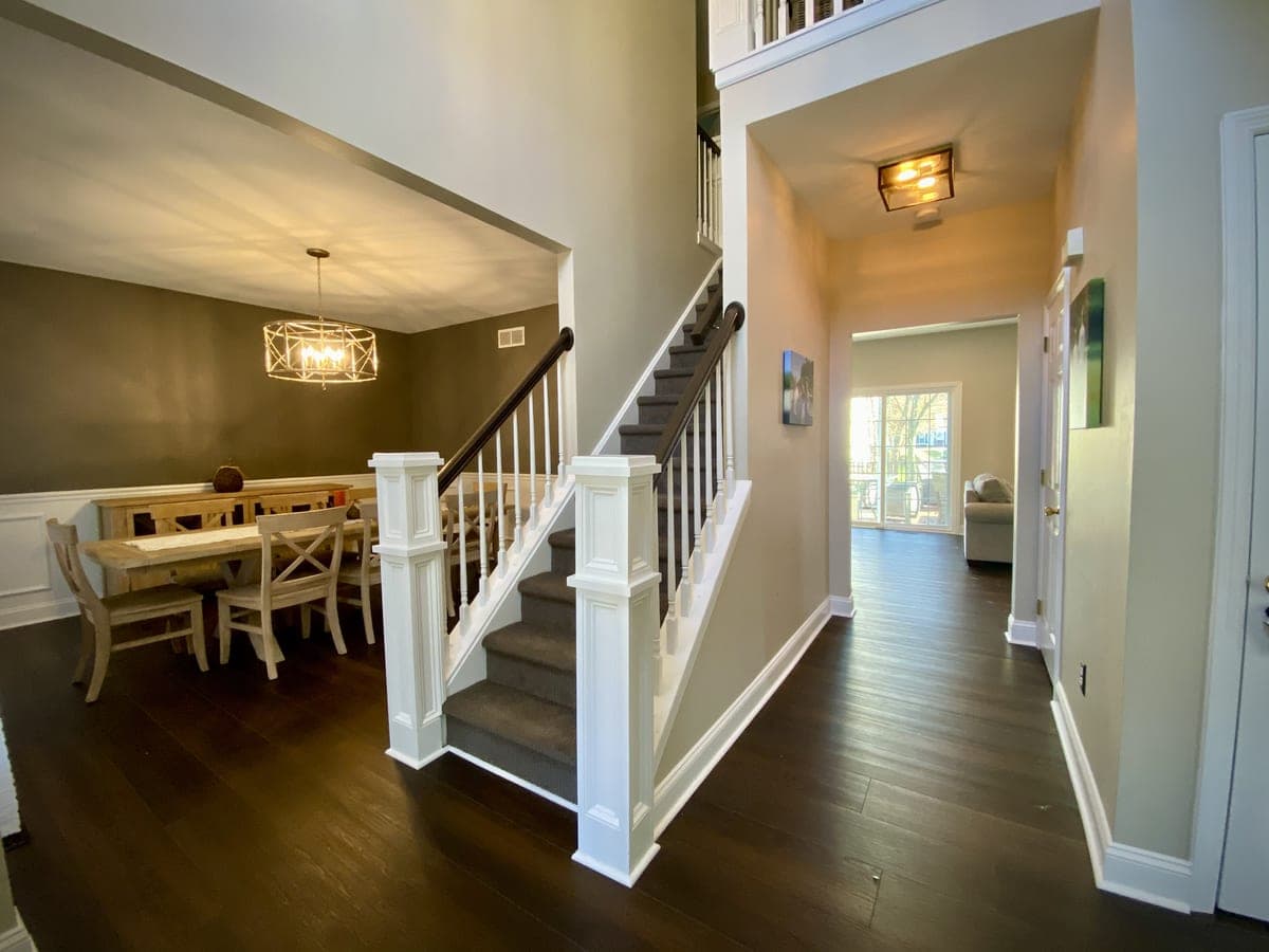 Entry and stair with greige walls, white rail, dining room with dark accent wall beyond