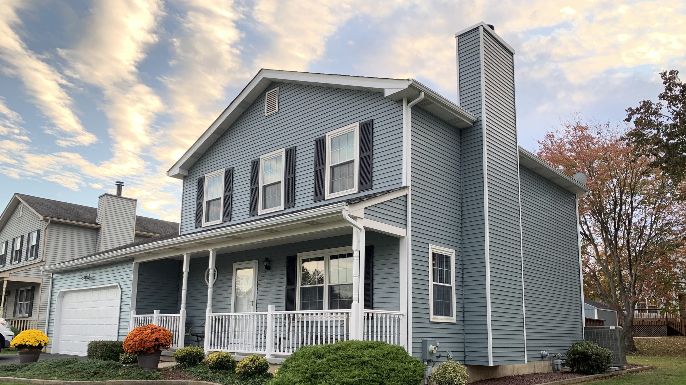 Blue-gray two-story with white porch rail and black shutters at golden hour